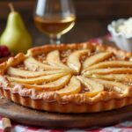 Rezeptidee Wein zum Essen Birnentarte mit Mandelcreme auf einem Holzbrett, begleitet von einem Glas Riesling