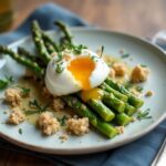 Rezeptidee Wein zum Essen Gebratener grüner Spargel mit pochiertem Ei & Dinkel-Crunch auf hellem Teller mit Glas Weißwein