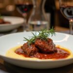 Rezeptidee Wein zum Essen Zarte Rinderbäckchen in Rotweinsauce mit cremiger Polenta, serviert mit einem Glas Primitivo