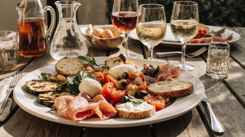 Kategoriebild Antipasti und Wein Italienische Antipasti-Platte mit gegrilltem Gemüse, Käse, Schinken und Weißwein auf rustikalem Holztisch im mediterranen Stil