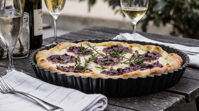 Rezeptidee Wein zum Essen Ziegenkäse Tarte mit Feigen und Rosmarin, serviert auf Holztablett mit Crémant im Glas im Garten