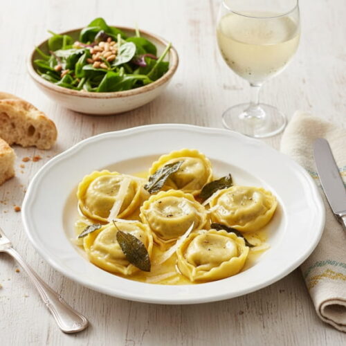 Wein zum Essen: Tortelloni di Magro in Salbeibutter neben einem Glas Pignoletto Weißwein.