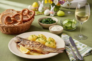 Eine gebratene Forelle Müllerin Art mit Mandeln und Kartoffeln neben einem Glas Weißburgunder.