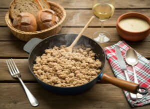 Wein zum Essen: Herzhafter Heidensterz mit Grammeln neben einem Glas Gelber Muskateller Wein.