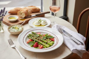 Spargel-Erdbeer-Salat mit Balsamico-Reduktion, frischer Minze und Pinienkernen auf weißem Porzellan, daneben ein Roséglas, Pariser Bistro-Setting