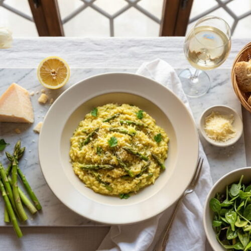 Spargelrisotto mit grünem Spargel und Zitronengremolata in cremefarbenem Teller, Soave Classico Weißweinglas, norditalienisches Marmor-Setting