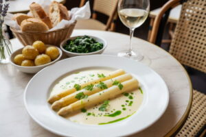 Weißer Spargel Sous-vide mit Beurre Blanc und Kräuteröl, Nahaufnahme auf cremefarbenem Teller, Pariser Bistro-Setting