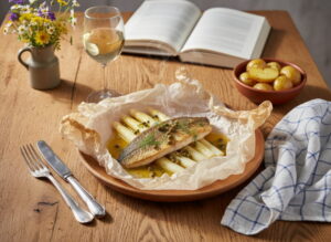 Weißer Spargel mit Zander en papillote und Kapernbutter, Päckchen geöffnet auf weißem Teller, Riesling Weißweinglas, bayerischer Bauerntisch